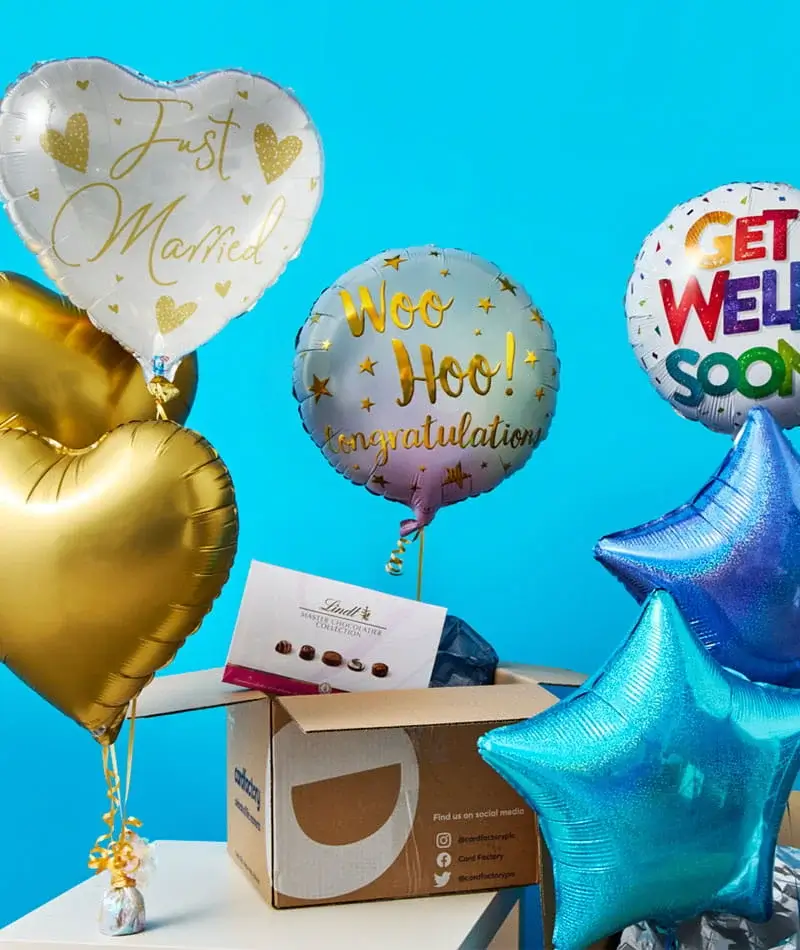 A selection of colourful celebration balloons, including Just Married, Congratulations, and Get Well Soon designs, displayed beside an open delivery box.